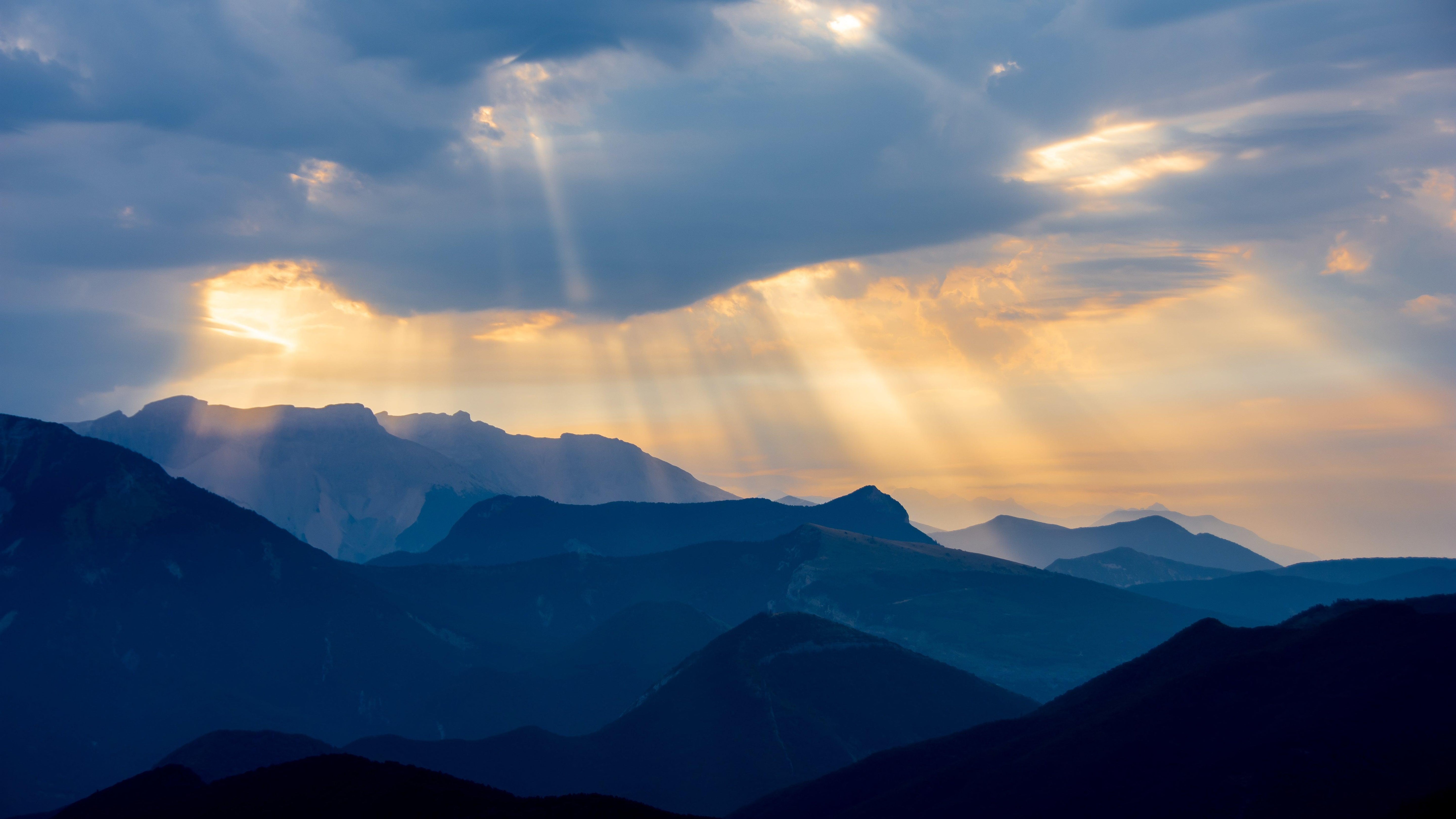 Coucher de soleil sur les montagnes avec rayons de lumière dorés traversant les nuages, paysage naturel écoresponsable.